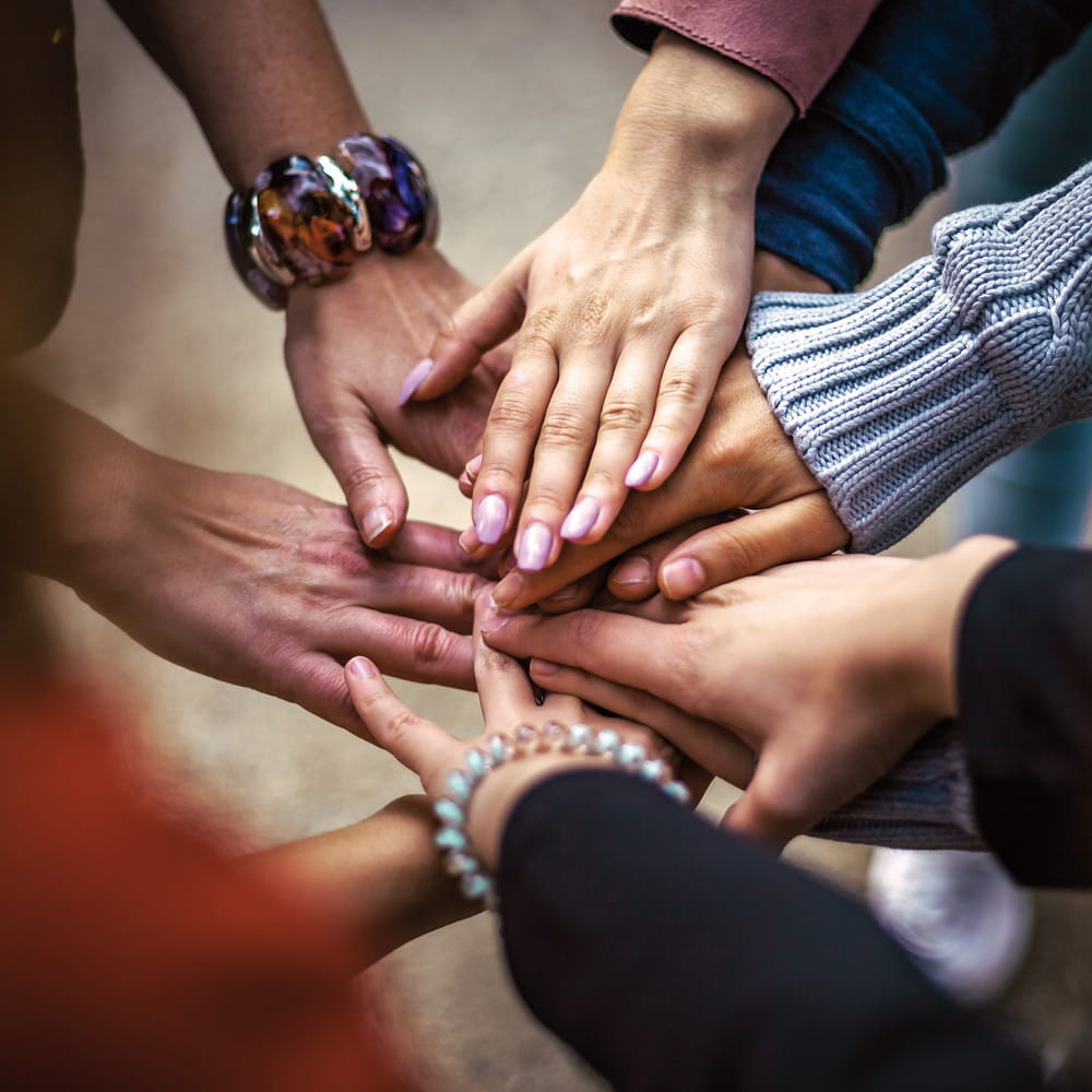 Mehrere Hände von Teammitgliedern liegen als Zeichen von Gemeinschaft und Solidarität übereinander.