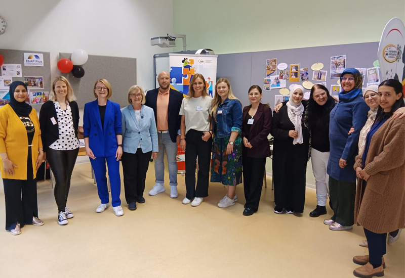 Ein Gruppenfoto mit dreizehn Personen welche im Halbkreis stehen und in die Kamera lachen