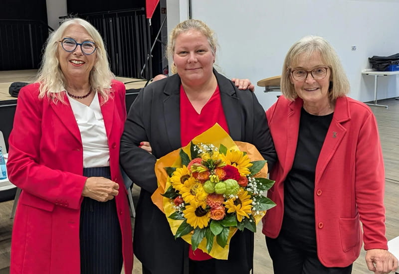 Nadine Ruf, Vorsitzende der AWO Wiesbaden, steht mit Blumenstrauß zwischen zwei Begleiterinnen bei einer offiziellen Veranstaltung