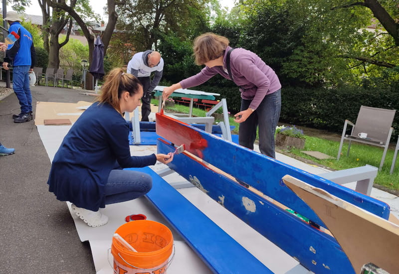 Engagierte Helfer streichen gemeinsam eine Sitzbank im Außenbereich bei Wiesbaden Engagiert