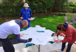 Mehrere freiwillige Helfer bemalen ein großes Holzobjekt im Außenbereich während Wiesbaden Engagiert