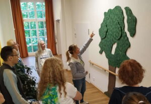 Gruppe betrachtet eine neu installierte Baum-Wandgestaltung im Innenbereich einer Einrichtung in Wiesbaden
