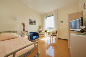 Helles Bewohnerzimmer im AWO Pflegezentrum Konrad Arndt mit Pflegebett, Sitzgelegenheit und großem Fenster mit Blick ins Grüne