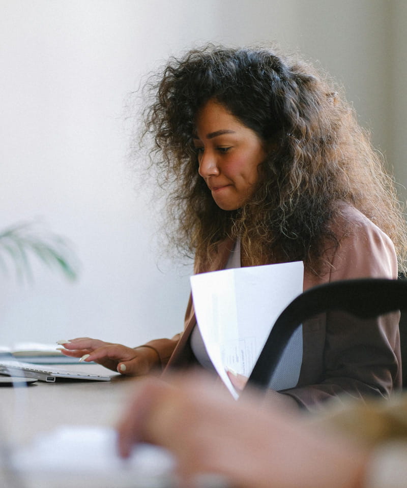Eine junge Frau mit lockigem Haar arbeitet konzentriert an einem Laptop und hält Dokumente in der Hand – Symbol für berufliche Entwicklung bei der AWO