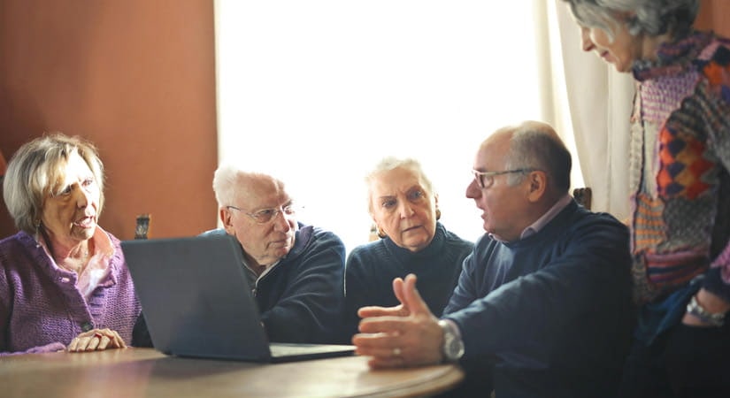 Austausch und digitale Unterstützung Mehrere Menschen sitzen gemeinsam an einem Tisch mit einem Laptop und sprechen miteinander