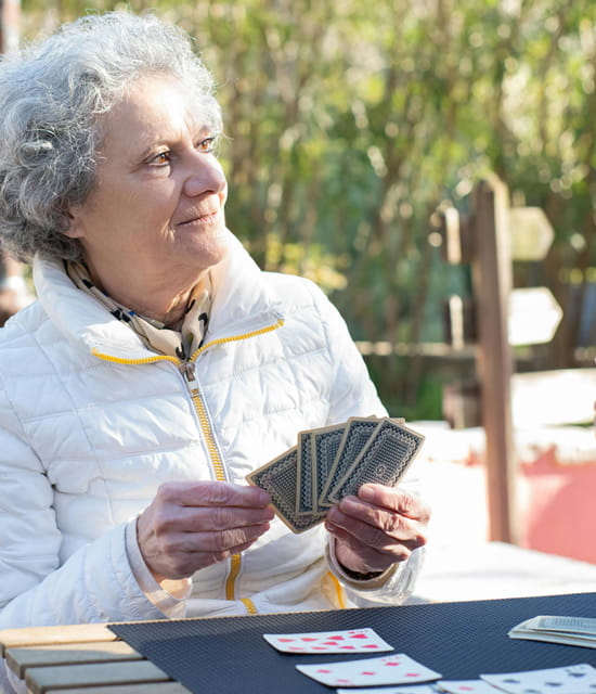 Gemeinsames Kartenspiel im Freien Frau sitzt im Freien an einem Tisch und hält Spielkarten in der Hand