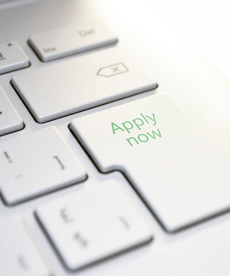 Nahaufnahme einer weißen Computertastatur, auf deren Enter-Taste in grüner Schrift „Apply now“ steht – Aufforderung zur Online-Bewerbung