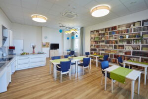 Heller Gemeinschaftsraum im Robert Krekel Haus mit Küchenbereich, Tischen, Stühlen und dekorativer Bücherwand