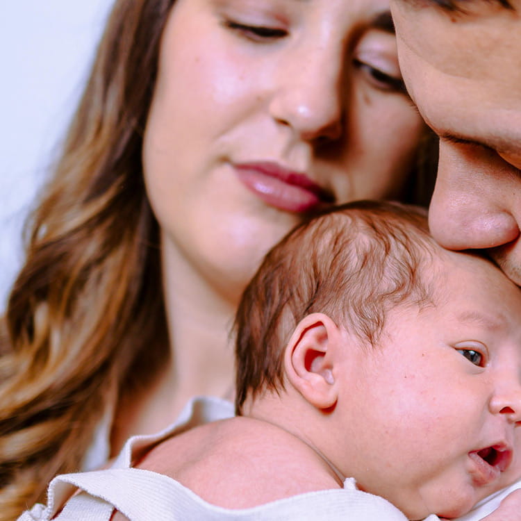 Eltern halten ihr Baby liebevoll im Arm und zeigen Nähe, Schutz und familiäre Geborgenheit