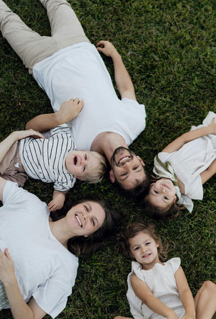 Familie liegt gemeinsam auf einer Wiese und blickt entspannt in die Kamera