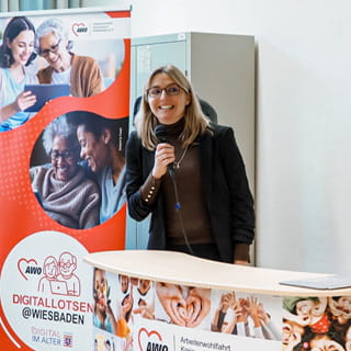 Eine Frau spricht bei der Vorstellung des Projekts Digitallotsen in Wiesbaden vor einem Roll Up Banner