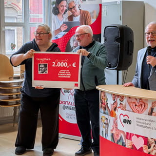 Zwei Personen präsentieren beim Kick Off der Digitallotsen in Wiesbaden einen symbolischen Spendenscheck über 2.000 Euro