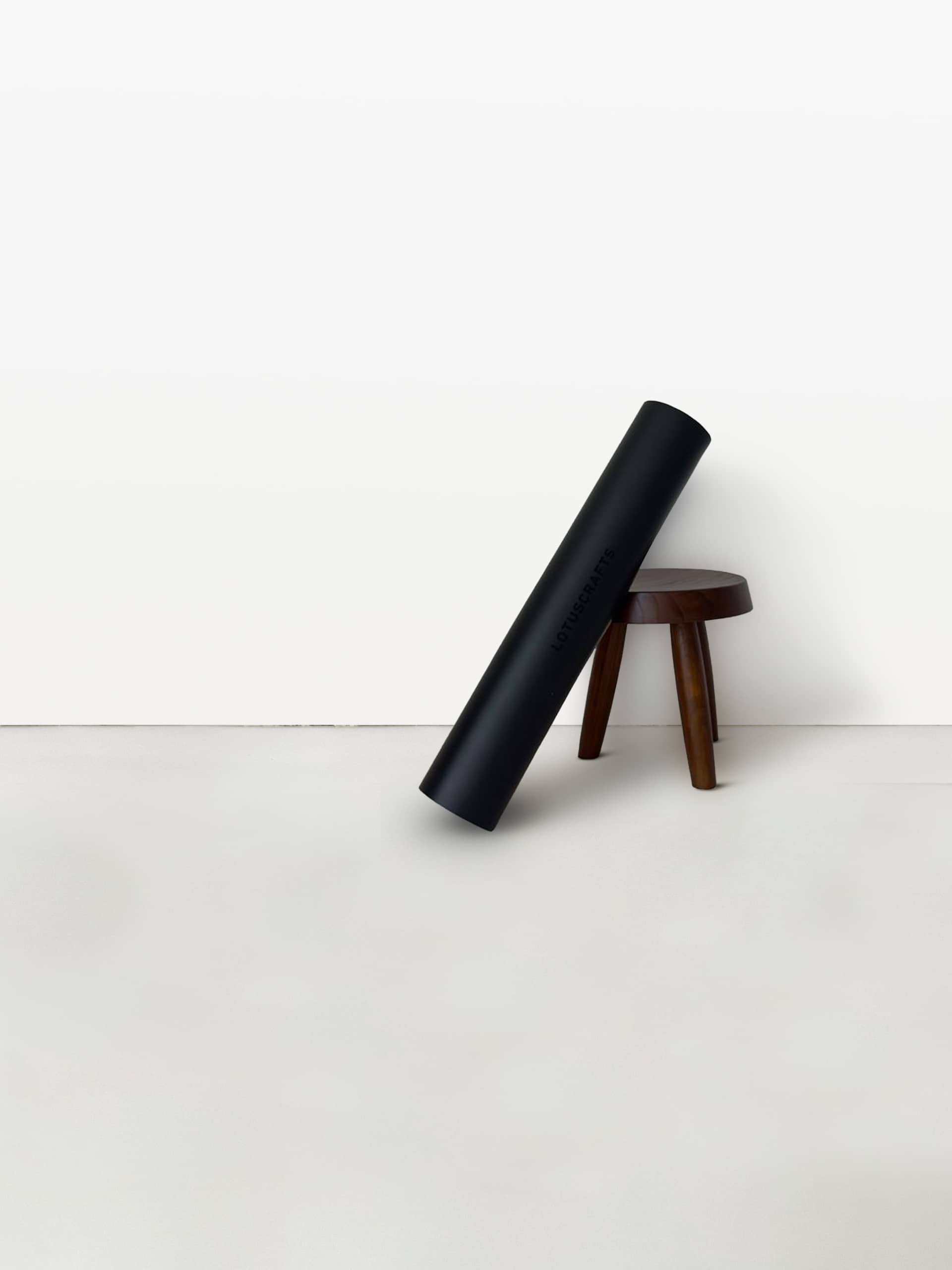 hwarze Yogamatte lehnt schräg an einem kleinen Holzhocker vor einer hellen Wand
