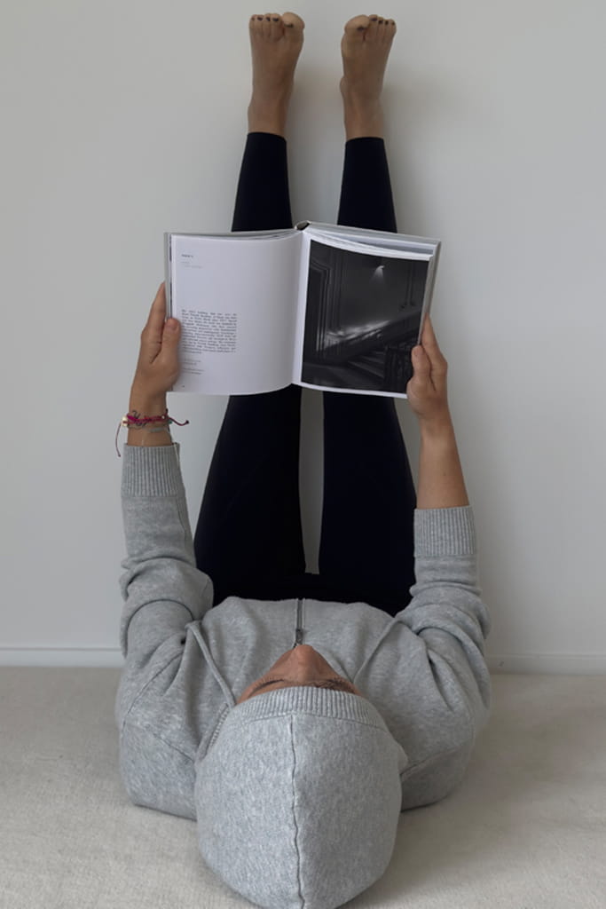 Frau liegt mit den Beinen an der Wand und liest ein aufgeschlagenes Buch