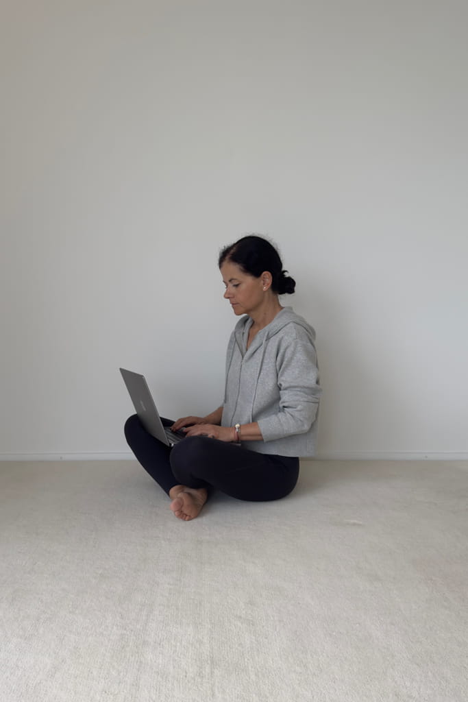 Frau sitzt im Schneidersitz auf dem Boden und arbeitet an einem Laptop