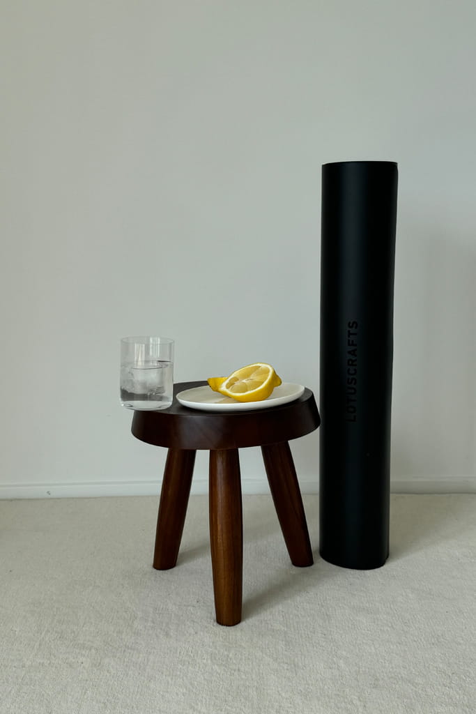 Schwarze Yogamatte steht neben einem Holzhocker mit einem Glas Wasser und Zitronen auf einem Teller